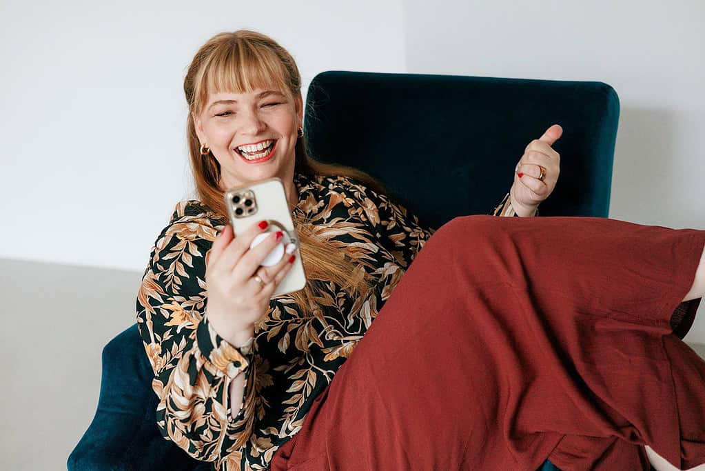 Fröhliche Frau mit Smartphone, Elternmagnet, Elternmarketing, Familie, Social Media, Authentisch, Emotionen, Online-Marketing, Elternbindung, Hassliebe Marketing.