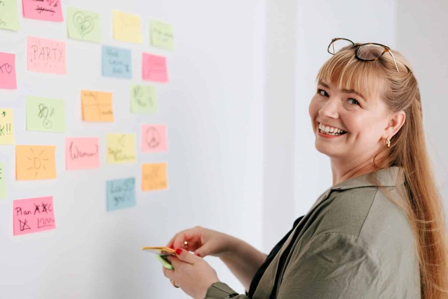 Fröhliche Frau mit Post-its am Whiteboard, Elternmagnet für Unterstützung bei Eltern-Kind-Organisationen.